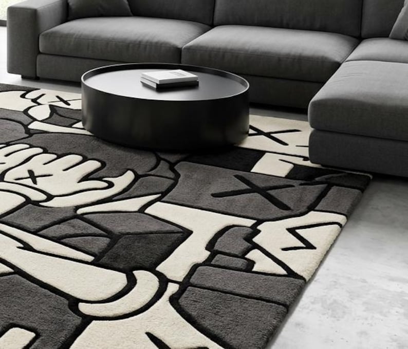 May include: A modern living room featuring a gray sectional sofa, a black round coffee table, and a patterned area rug. The rug has a repeating design in black, white, and gray.