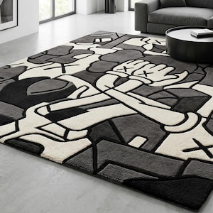May include: A large, rectangular area rug with a modern design. The rug features a repeating pattern of abstract figures in shades of gray, black, and off-white. The design includes stylized hands with crossbones. The rug is placed on a concrete floor.