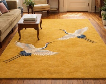 May include: Mustard yellow rectangular rug with two embroidered cranes. The cranes have white wings, blue and black details, and long legs. The rug is placed on a wooden floor. The rug's dimensions are in centimetres.