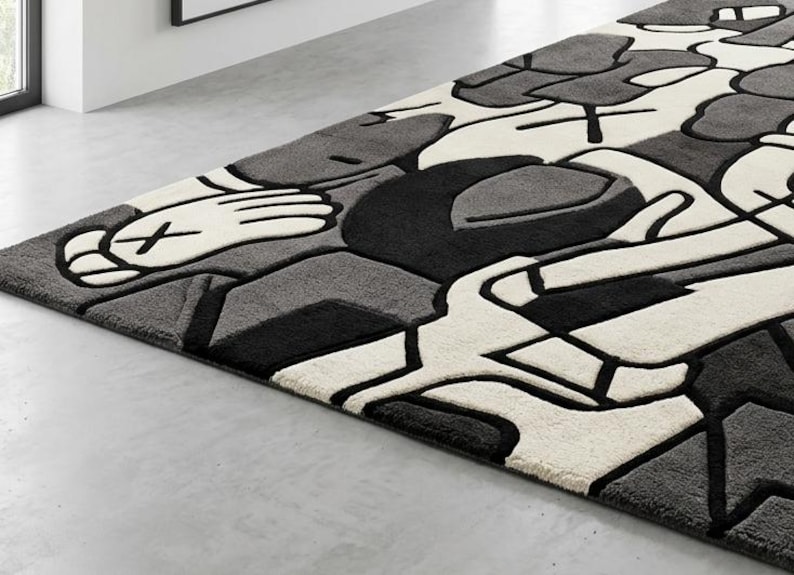 May include: A rectangular area rug with a modern design. The rug features a pattern of abstract shapes in shades of gray, black, and white. The design includes stylized hands and geometric forms, creating a contemporary aesthetic. The rug is placed on a light gray floor.