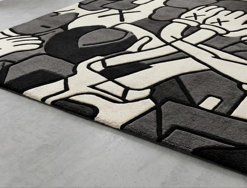 May include: A rectangular rug with a modern, abstract design in shades of black, gray, and white. The rug features a geometric pattern with thick black outlines and a plush texture. The design includes stylized hands and shapes.