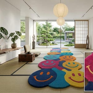 Puede incluir: Una colorida alfombra con una serie de caras sonrientes en varios colores, incluyendo azul, rosa, amarillo y naranja. La alfombra está colocada en una habitación con un diseño minimalista, con grandes ventanales y vistas a un jardín.