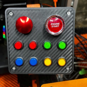 May include: A black control panel with a carbon fiber texture. It features a large red button and an "ENGINE START" button. There are eight smaller buttons in red, green, blue, and yellow. The panel is secured with four screws.
