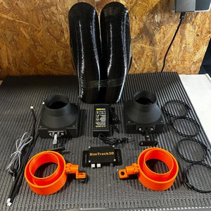 May include: An assortment of black and orange automotive parts, including two black flexible tubes, two black fan housings, two orange circular mounts, and a SimTrack3D control module. Additional components include a power supply and several black hose clamps.