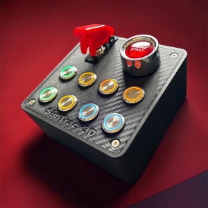 May include: A black carbon fiber textured button box for simulation racing featuring a red flip-up safety switch, a large red Engine Start button, and seven smaller circular push buttons with illuminated rings in green, yellow, and blue.