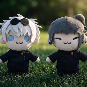 Könnte beinhalten: Zwei Plüschpuppen von Anime-Charakteren. Eine Puppe hat weißes Haar und eine schwarze Sonnenbrille, die andere hat dunkles Haar in einem Dutt. Beide Puppen tragen schwarze Jacken mit einem einzelnen goldenen Knopf. Sie haben lächelnde Gesichter und stehen auf grünem Gras.