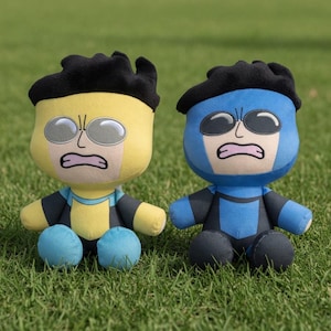 Può includere: Due bambole di peluche di un supereroe, una gialla e una blu, sono sedute sull'erba verde. Ogni bambola ha una copertura per la testa nera, occhi grandi e un'espressione facciale angosciata. Le bambole indossano abiti da supereroe.