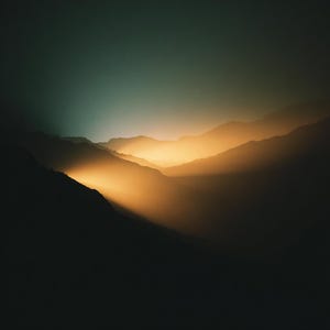Può includere: Fotografia di paesaggio di catene montuose. L'immagine presenta una sfumatura di colori, con un cielo verde scuro che passa a una luce dorata e calda che illumina le valli. Le sagome delle montagne creano un contrasto drammatico.
