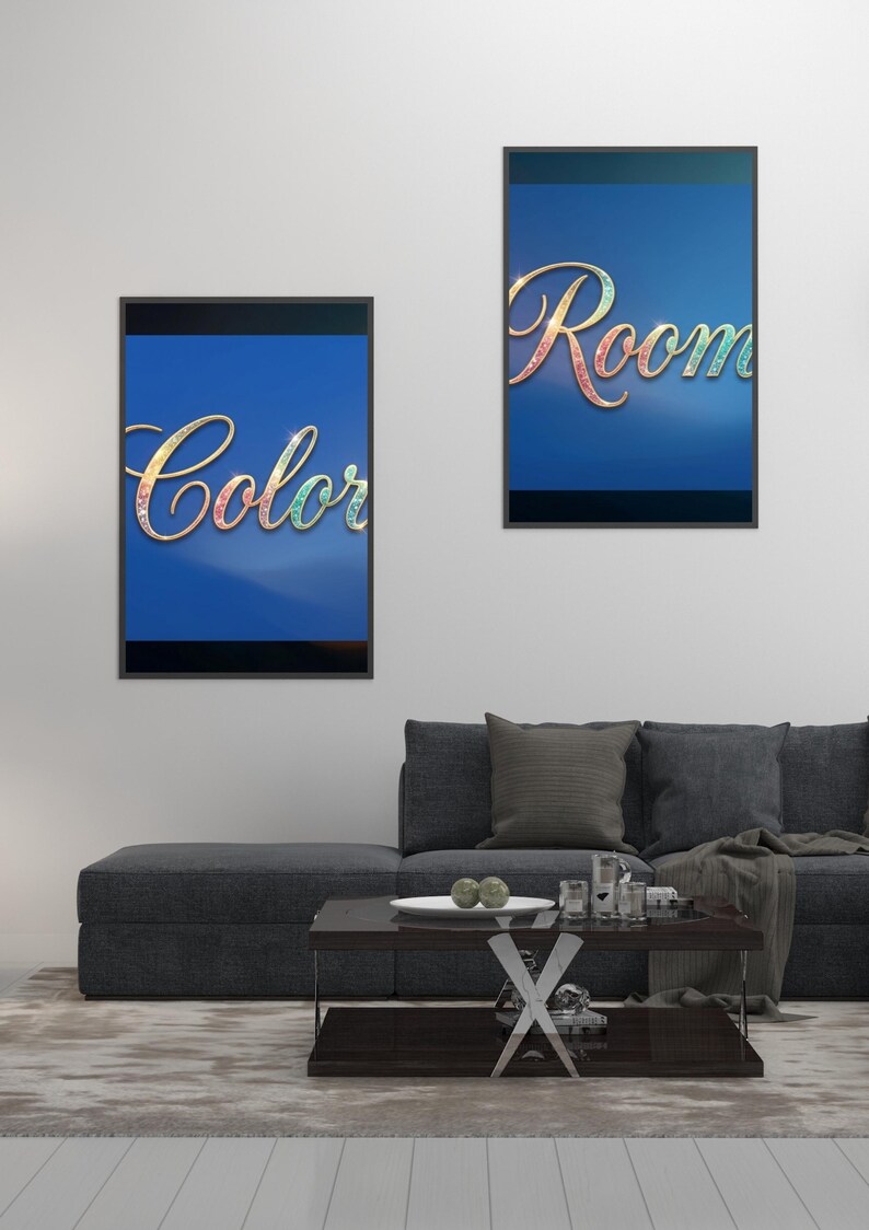May include: Two framed art prints with the words "Color" and "Room" in a decorative font. The words have a colorful, iridescent effect against a blue background. The prints are displayed above a gray sofa.