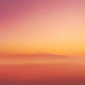 May include: An abstract landscape photograph featuring a gradient of colors. The sky transitions from a soft pink at the top to a warm orange and yellow towards the horizon. Silhouetted mountains are visible in the distance, with a hazy, reddish-orange foreground.