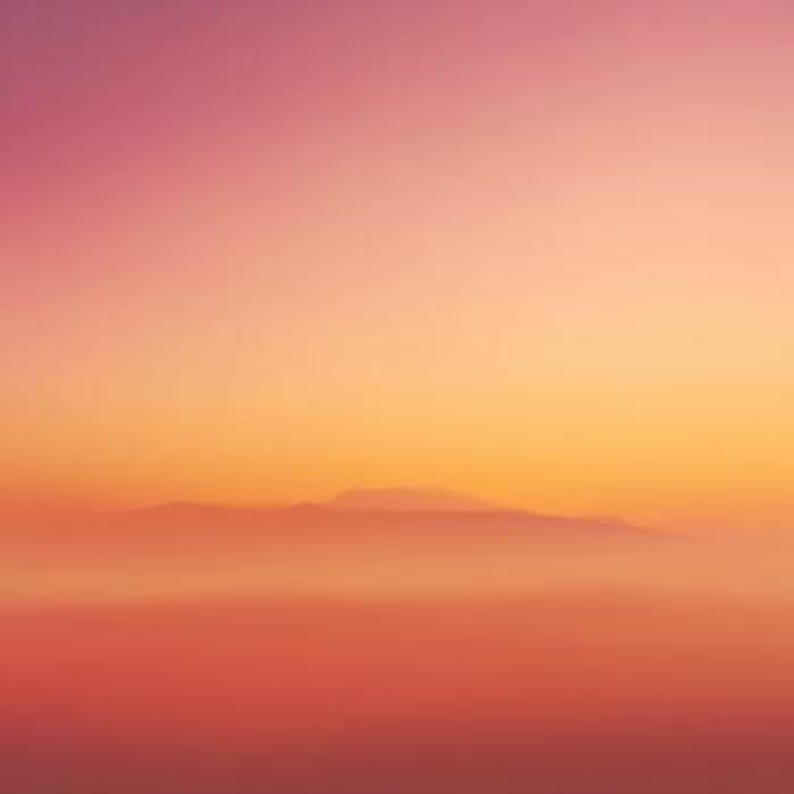 May include: An abstract landscape photograph featuring a gradient of colors. The sky transitions from a soft pink at the top to a warm orange and yellow towards the horizon. Silhouetted mountains are visible in the distance, with a hazy, reddish-orange foreground.