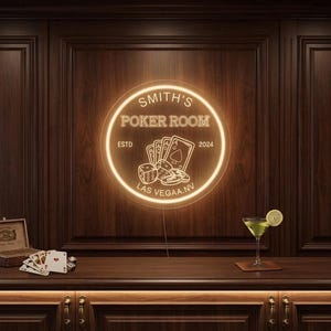 Op de afbeelding: Een rond neonbord voor "Smith's Poker Room" met pokersymbolen, waaronder speelkaarten en dobbelstenen. Het bord is bevestigd aan een donkere houten lambrisering. Een cocktail en speelkaarten liggen op de bar.