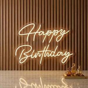 Puede incluir: Un letrero de neón blanco cálido que muestra las palabras Happy Birthday en una fuente cursiva. El letrero está montado en una pared de listones de madera verticales. Tres frascos de perfume de vidrio pequeños descansan sobre una base.