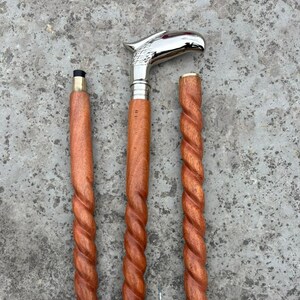 Könnte beinhalten: Ein hölzerner Spazierstock mit einem silbernen Adlerkopfgriff. Der Stock ist in drei Teile zerlegt, mit einem gedrehten Holzdesign. Die Gesamtlänge des Stocks beträgt ca. 94 cm im zusammengebauten Zustand.