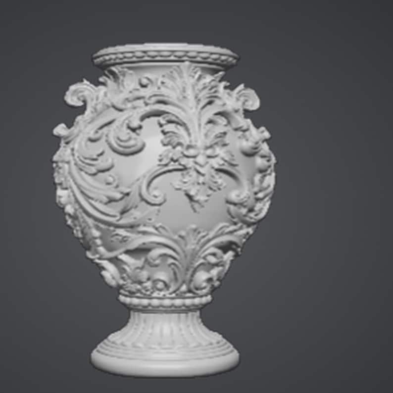 May include: A white, ornate vase with a detailed floral and scroll design. The vase has a wide, rounded body, a pedestal base, and a decorative rim. The intricate carvings and symmetrical composition give it a classic, elegant appearance.
