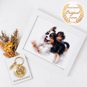 May include: A white framed print featuring a watercolor painting of a black, white, and brown dog with its mouth open. Beside the frame is a gold-toned circular metal keychain engraved with a dog portrait and the name Miko on a tag.
