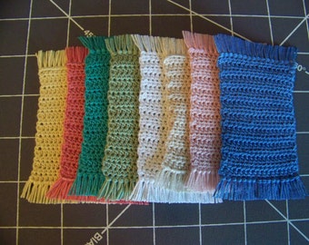 Puede incluir: Un conjunto de ocho alfombras de crochet en varios colores, incluyendo amarillo, rojo, verde, beige, blanco, rosa y azul. Cada alfombra tiene un borde de flecos.