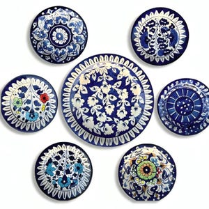 Może przedstawiać: Zestaw siedmiu dekoracyjnych ceramicznych talerzy z misternymi niebiesko-białymi wzorami kwiatowymi. Talerze, o różnych rozmiarach, prezentują różnorodne style artystyczne. Ułożone na białym tle.