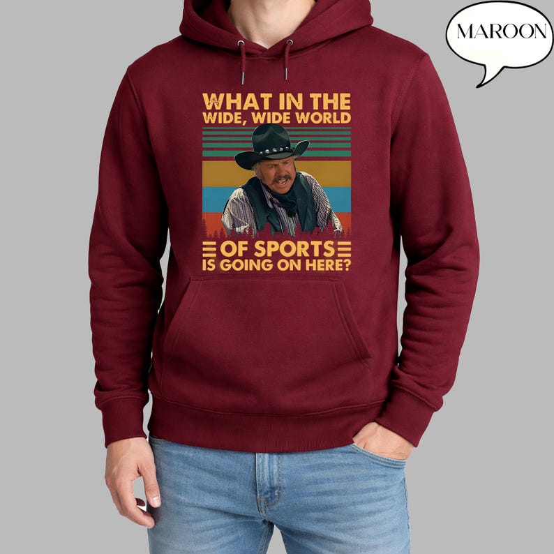 May include: Maroon hoodie with a graphic featuring a man in a cowboy hat and the text "WHAT IN THE WIDE, WIDE WORLD OF SPORTS IS GOING ON HERE?". The word "MAROON" is in a speech bubble.