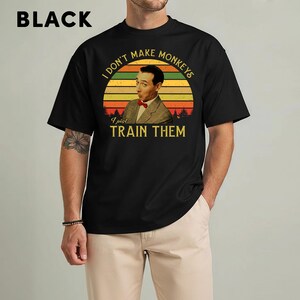 May include: Black t-shirt featuring a retro design with the text "I don't make monkeys, I just train them." The graphic includes a portrait of a man in a suit and bow tie set against a sunset background. The word "BLACK" is at the top.
