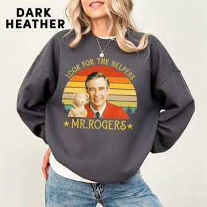 May include: Dark heather gray sweatshirt featuring a graphic of Mr. Rogers with a puppet and the text "Look for the Helpers" and "Mr. Rogers" in a retro design. The sweatshirt has long sleeves.