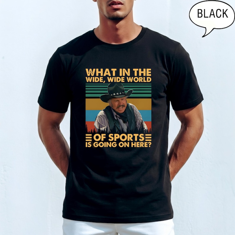 May include: Black t-shirt with a graphic featuring a man in a cowboy hat and the text "WHAT IN THE WIDE, WIDE WORLD OF SPORTS IS GOING ON HERE?". The design includes a retro color scheme with blue, green, and orange stripes.