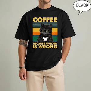 May include: Black t-shirt with a graphic featuring a black cat holding a coffee cup. The text reads "COFFEE BECAUSE MURDER IS WRONG" in yellow and white. The design has a retro color block background.