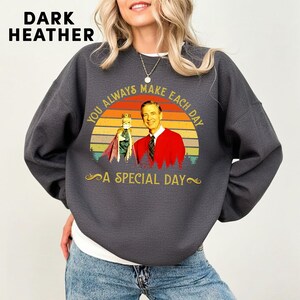 May include: Dark heather gray sweatshirt with a graphic of a man in a red jacket and a puppet, set against a sunset design. Text reads "YOU ALWAYS MAKE EACH DAY A SPECIAL DAY".