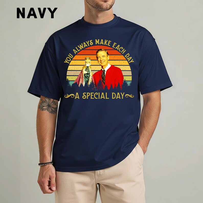 May include: Navy blue t-shirt featuring a graphic of a man in a red sweater and a puppet, set against a sunset backdrop. The text reads "You Always Make Each Day A Special Day". The word "NAVY" is printed at the top left.