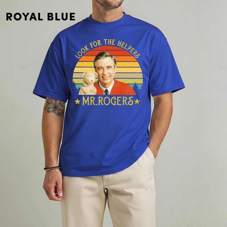 May include: Royal blue t-shirt featuring a graphic of Mr. Rogers with a cat and the text "LOOK FOR THE HELPERS" and "MR.ROGERS" in a vintage style. The shirt is a solid royal blue color.