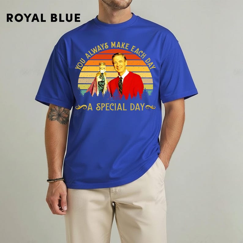 May include: Royal blue t-shirt with a graphic featuring a vintage image of a man in a red jacket and a puppet, set against a sunset backdrop. Text reads "YOU ALWAYS MAKE EACH DAY A SPECIAL DAY".