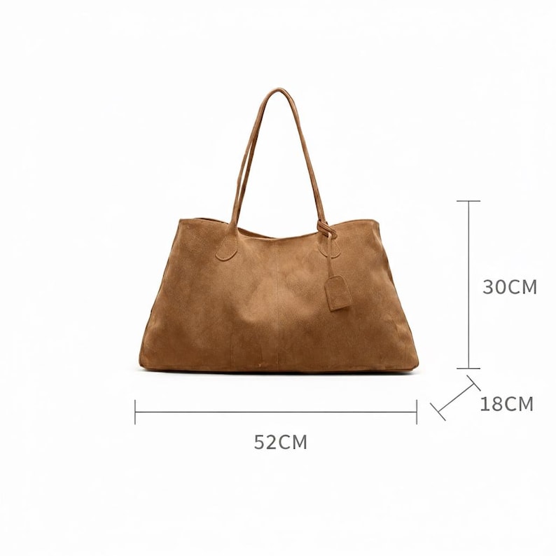 May include: A large, brown suede tote bag with long handles and a small tag. The bag measures 20.5 inches long, 11.8 inches high, and 7 inches wide. The bag is a neutral color and has a simple, classic design.