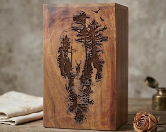 May include: A wooden box with a carved design of a person walking through a forest, with a deer and birds. The box is rectangular and made of a light brown wood.