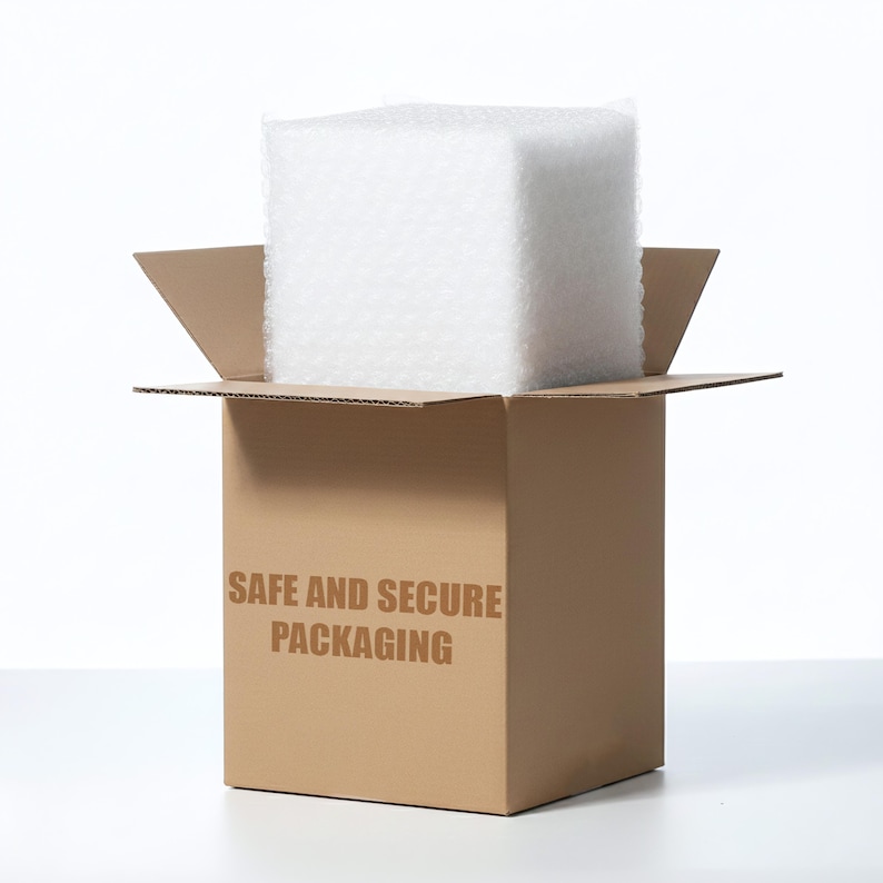 Puede incluir: Una caja de env&iacute;o de cart&oacute;n marr&oacute;n con solapas abiertas, que contiene un gran bloque cuadrado de pl&aacute;stico de burbujas blanco. El frente de la caja presenta el texto SAFE AND SECURE PACKAGING impreso en una fuente negrita, marr&oacute;n y sin remates.