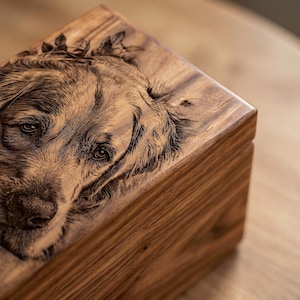 May include: A rectangular wooden box featuring a detailed laser-engraved portrait of a golden retriever on the lid. The natural wood grain is visible across the surface, and the engraving captures the dog's facial features and fur texture.