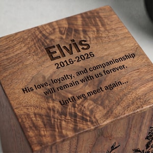 Puede incluir: Una caja cuadrada de madera con un acabado de veta de madera marr&oacute;n oscuro. La superficie superior est&aacute; grabada con el nombre Elvis, las fechas 2016-2026 y el texto: His love, loyalty, and companionship will remain with us forever. Until we meet again...