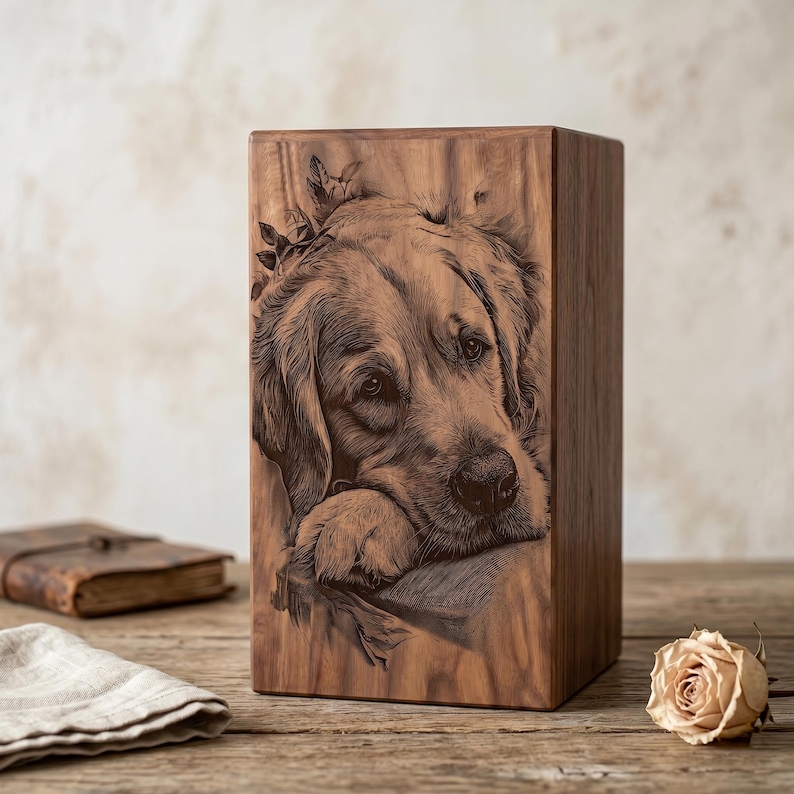 May include: A rectangular wooden urn featuring a detailed laser-engraved portrait of a golden retriever resting its head on its paws. The natural wood grain is visible across the surface, showcasing a warm brown tone and a smooth, polished finish.