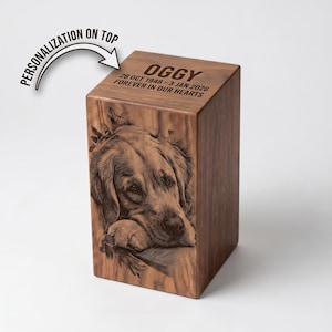 May include: A rectangular wooden urn featuring a laser-engraved portrait of a dog on the front panel. The top surface is engraved with the name OGGY, the dates 28 OCT 1948 - 3 JAN 2026, and the text FOREVER IN OUR HEARTS. A graphic arrow points to the top.