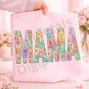 May include: A light pink tote bag with the word "MAMA" in large, colorful, floral-filled letters. The flowers are in shades of pink, yellow, blue, and purple. The bag is held up by a person.