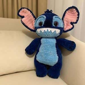 Puede incluir: Un peluche hecho a mano del personaje Stitch de la película Lilo & Stitch. El juguete es principalmente azul oscuro con detalles en azul claro y rosa. Tiene orejas grandes, una gran sonrisa y ojos grandes. El juguete mide aproximadamente 25 cm de alto.