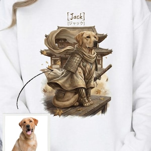 Może przedstawiać: Biała bluza z nadrukiem złotego retrievera w zbroi samuraja, trzymającego katanę. Projekt zawiera japońską świątynię i opadające liście. Imię "Jack" jest wydrukowane w języku angielskim i japońskim.