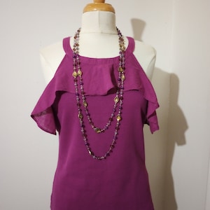 May include: A magenta sleeveless top with a ruffled neckline and a layered beaded necklace with gold and purple accents.