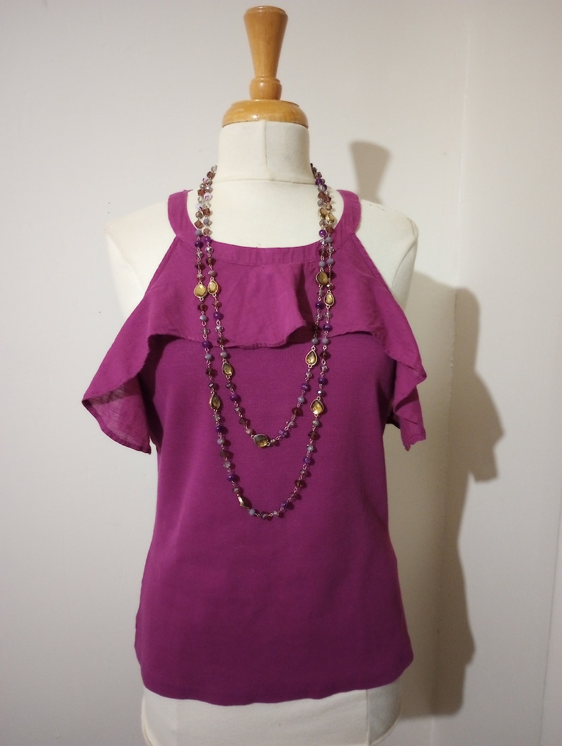 May include: A magenta sleeveless top with a ruffled neckline and a layered beaded necklace with gold and purple accents.