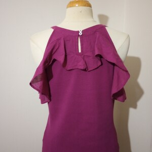May include: A magenta sleeveless top with a ruffled neckline and a button closure at the back.
