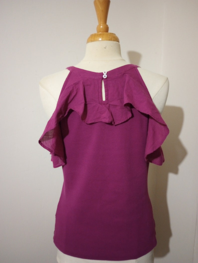 May include: A magenta sleeveless top with a ruffled neckline and a button closure at the back.