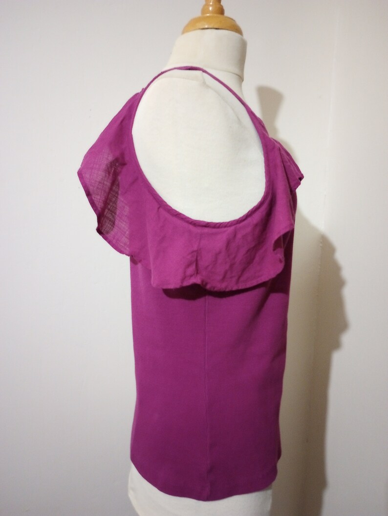 May include: A magenta sleeveless top with a ruffled neckline and a single strap. The top is made of a soft, lightweight fabric.