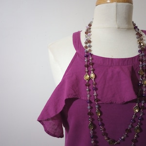 May include: A magenta sleeveless top with a ruffled neckline and a layered beaded necklace with purple, brown, and gold accents.