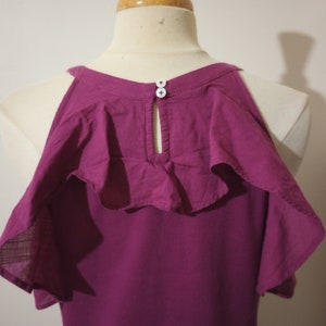 May include: A magenta cold shoulder top with ruffled sleeves and a button detail at the back of the neck.