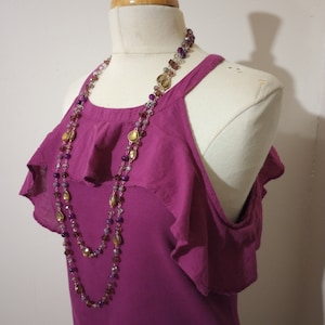 May include: A pink sleeveless top with a ruffled neckline and a layered necklace with gold and purple beads.