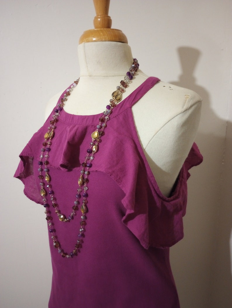 May include: A pink sleeveless top with a ruffled neckline and a layered necklace with gold and purple beads.